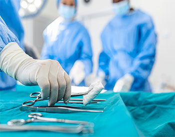 Nurse hand taking surgical instrument for group of surgeons at background operating patient in surgical theatre.